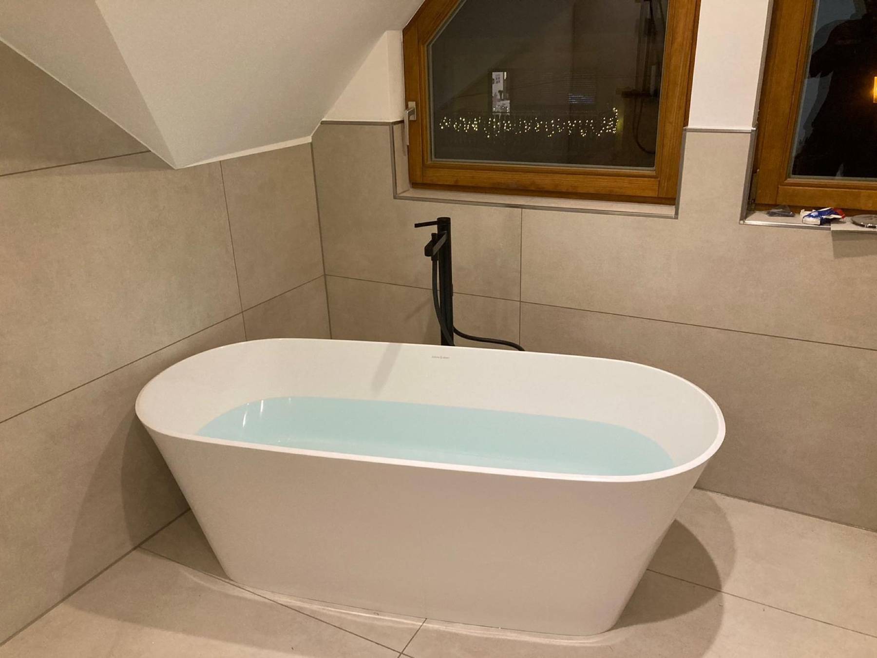 Freistehende Badewanne unter der Dachschräge mit schwarzer Standarmatur
